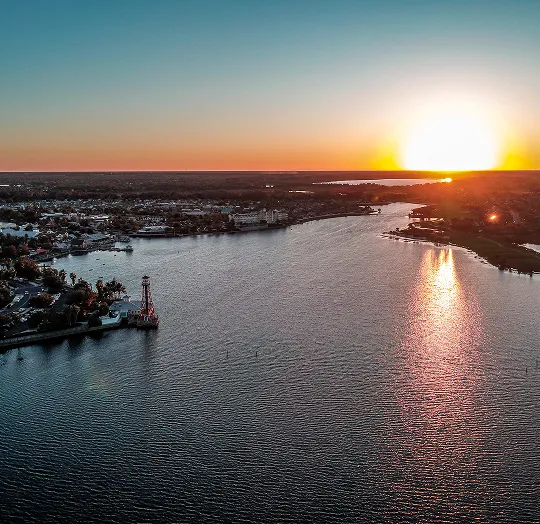 Aerial view of a river at sunset with a lighthouse on the left shoreline.