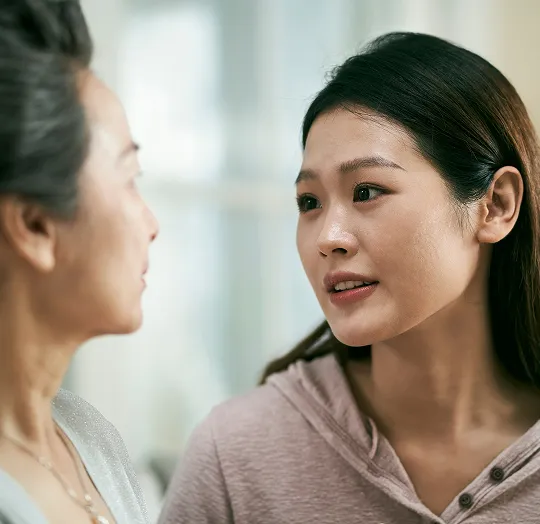 Two Asian women engaged in a serious conversation in a softly lit indoor setting.