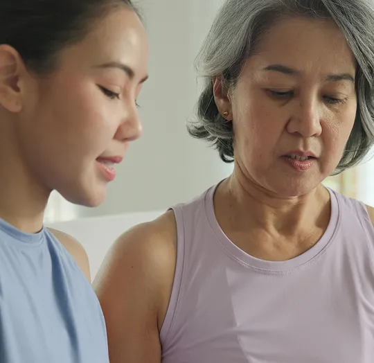Two women, one younger and one older with gray hair, wearing sleeveless tops indoors.