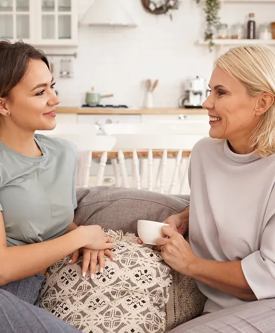 Two women engaged in conversation on a couch in a bright, modern kitchen.