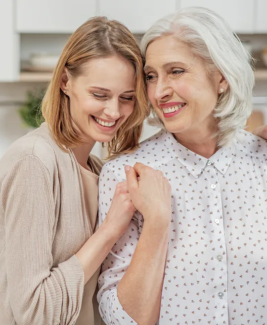 Two women, one younger and one older, smiling and embracing indoors.