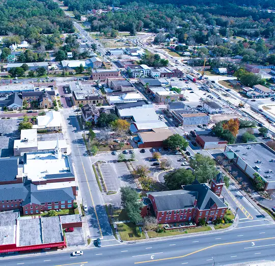 Aerial view of a small town with commercial buildings, streets, trees, and a prominent red brick clock tower.