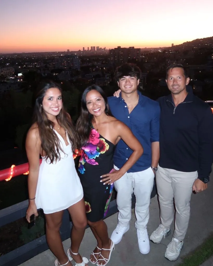 Four adults posing outdoors at sunset with city skyline in background, dressed in semi-formal attire.