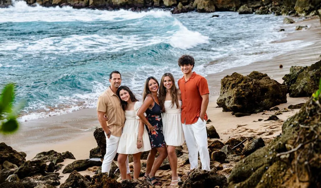 Five people standing on rocky beach shore with ocean waves in the background.