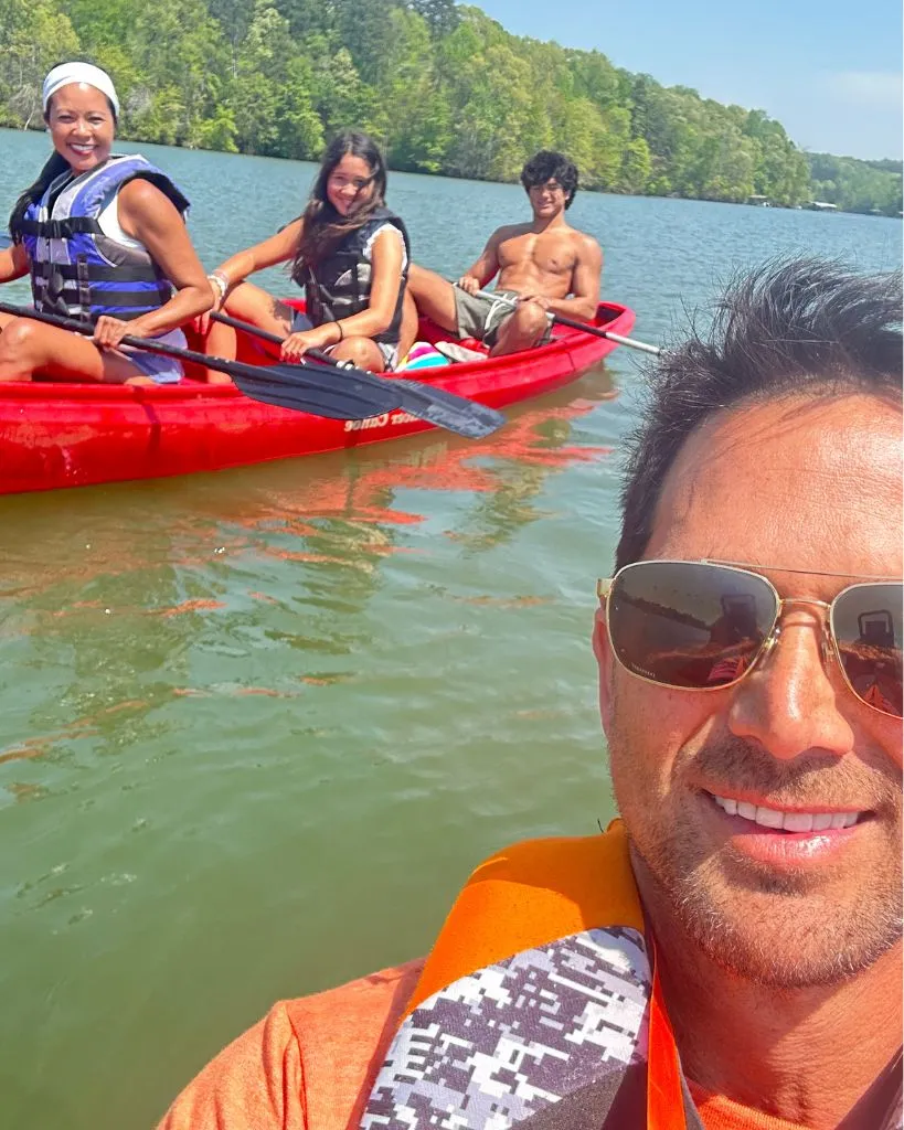 Group of four people enjoying a sunny day kayaking on a lake surrounded by green trees.