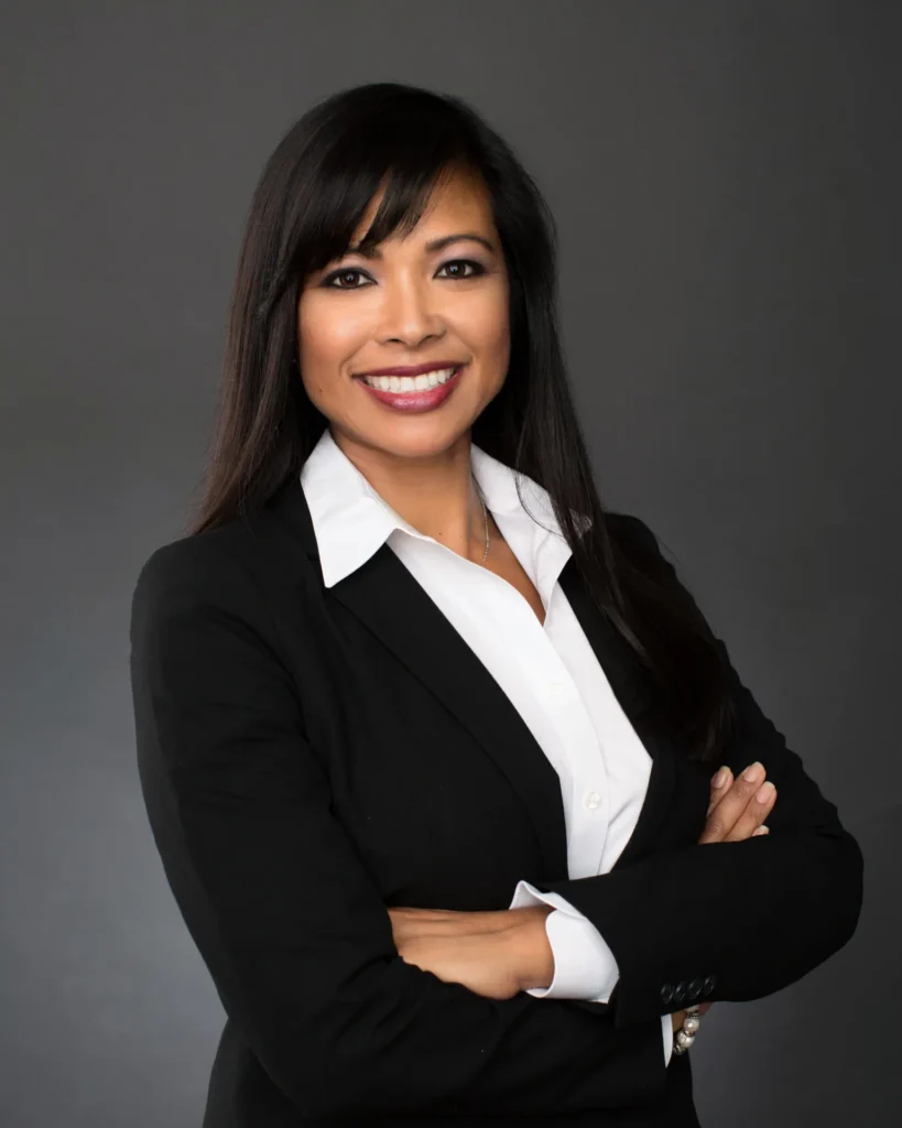 Professional portrait of a smiling woman with long black hair wearing a black blazer and white shirt.