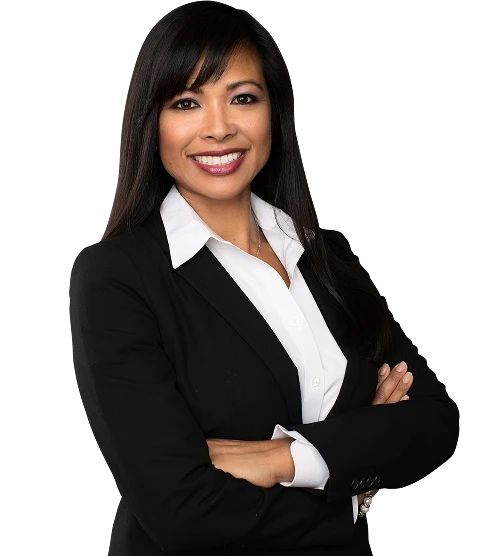 Professional woman with long dark hair wearing a black blazer and white shirt, smiling with arms crossed.