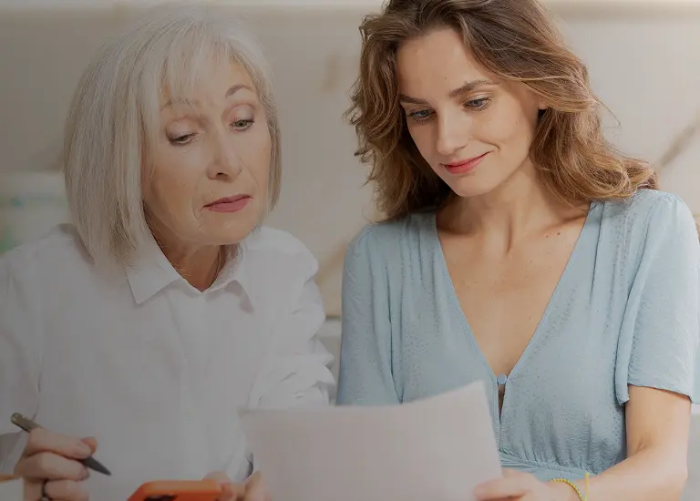 Two women, one older with gray hair and one younger with brown hair, reviewing a document together.