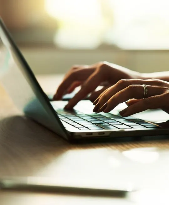 Close-up of hands typing on a laptop keyboard with natural light in the background.