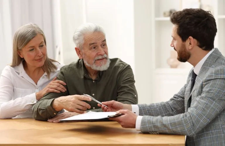 Elderly couple consulting a professional man in a gray suit with documents at a wooden table.