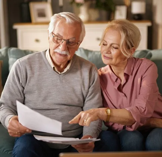 Elderly couple sitting on a sofa, reviewing documents together in a cozy living room.