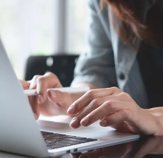 Close-up of a person typing on a silver laptop keyboard in a softly lit room.