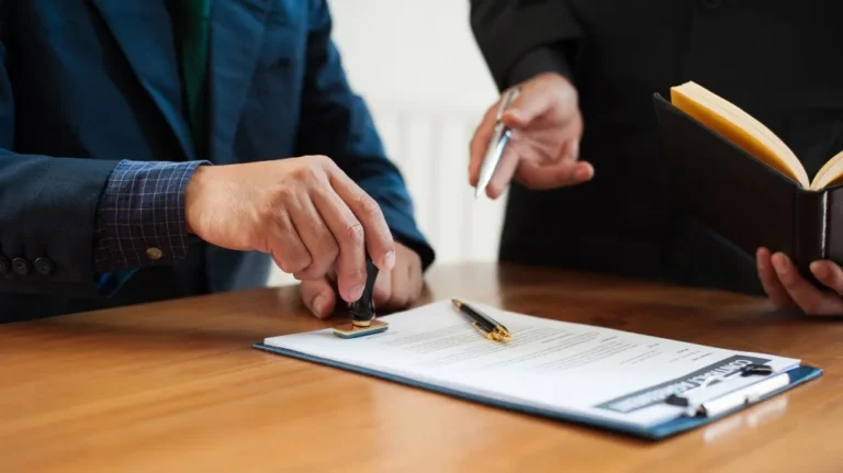 Two individuals in formal attire stamping and reviewing a contract on a wooden table.