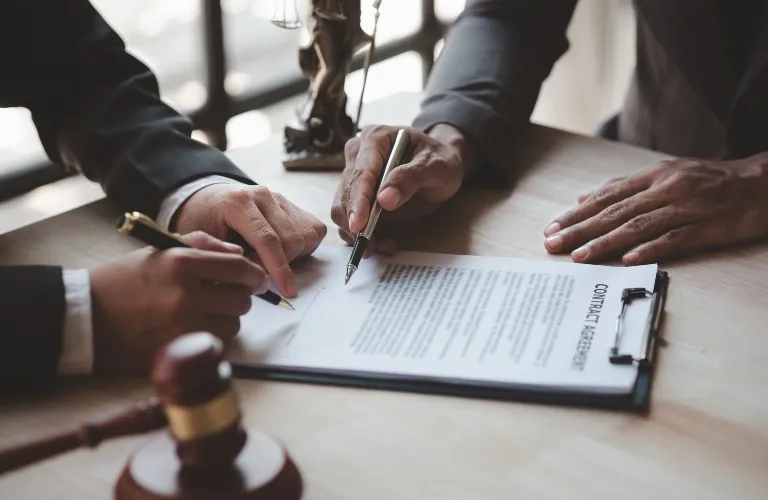 Two professionals in dark suits reviewing and signing a contract agreement document.