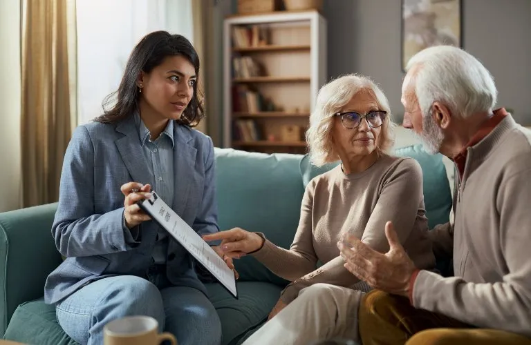 Professional woman in blue suit explaining document to elderly couple on sofa.