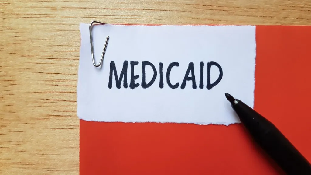 White paper with the word "MEDICAID" clipped by a paperclip on a red folder, black pen nearby.