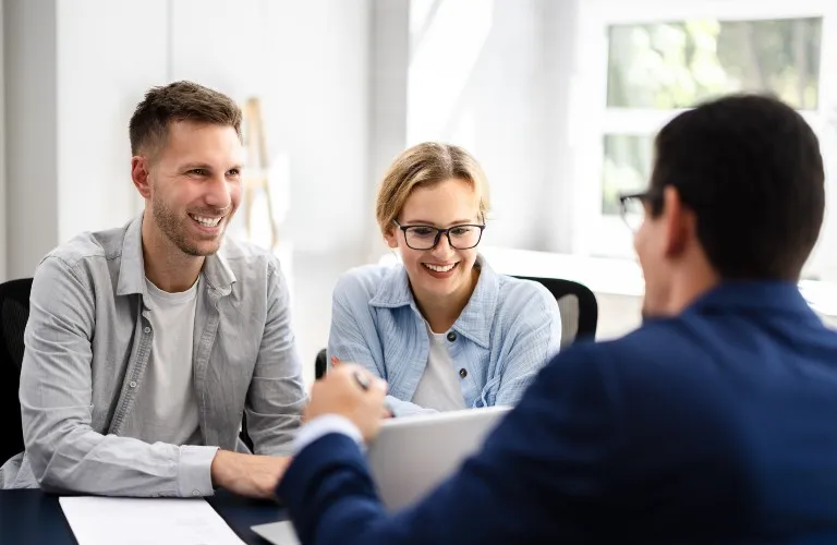 Two young professionals smiling during a consultation with a man in a navy suit at an office.