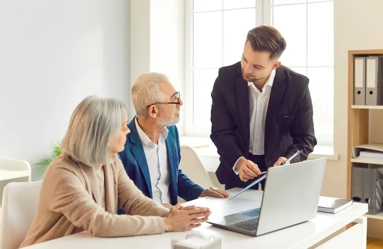 Three professionals engaged in discussion around a laptop in a bright office.