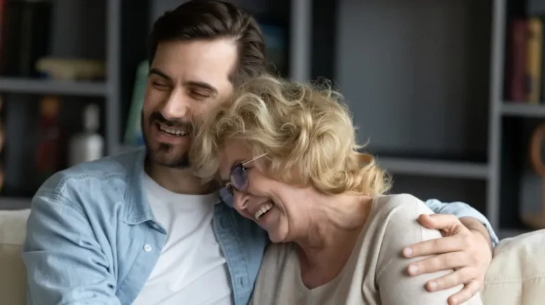 Middle-aged man and elderly woman smiling and embracing on a couch indoors.