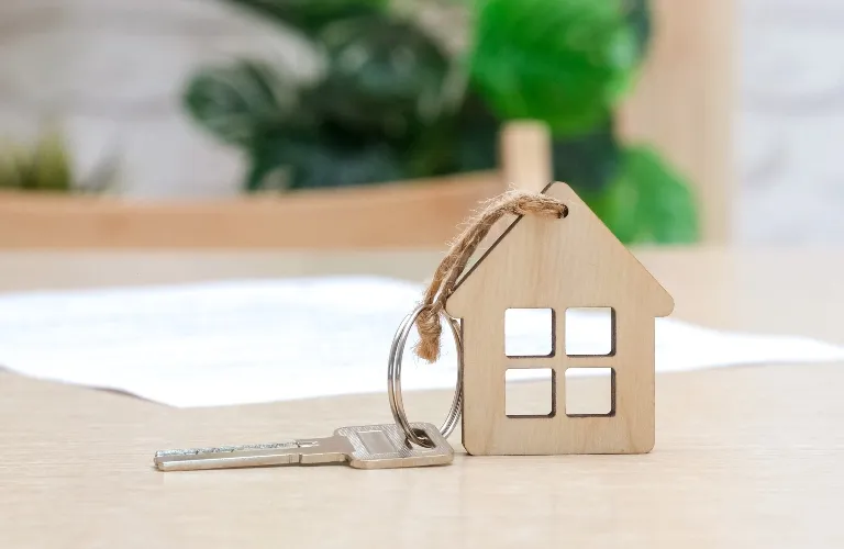 Small wooden house-shaped keychain attached to a silver key on a light wood table.