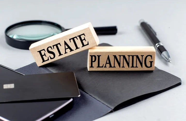 Wooden blocks with the words "ESTATE" and "PLANNING" alongside a pen, magnifying glass, and credit cards.