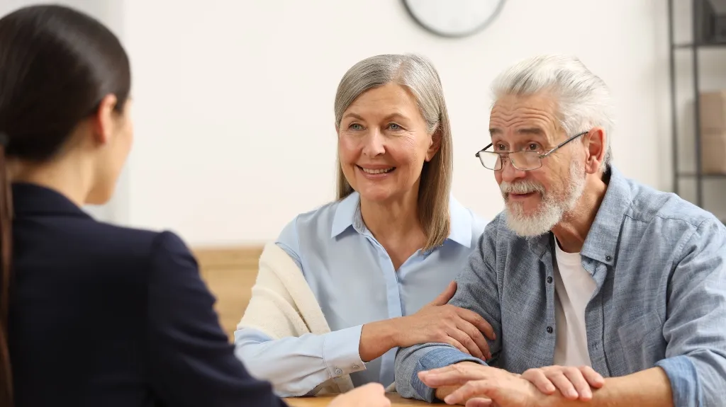 Elderly couple attentively listening to a younger professional woman in an office setting.